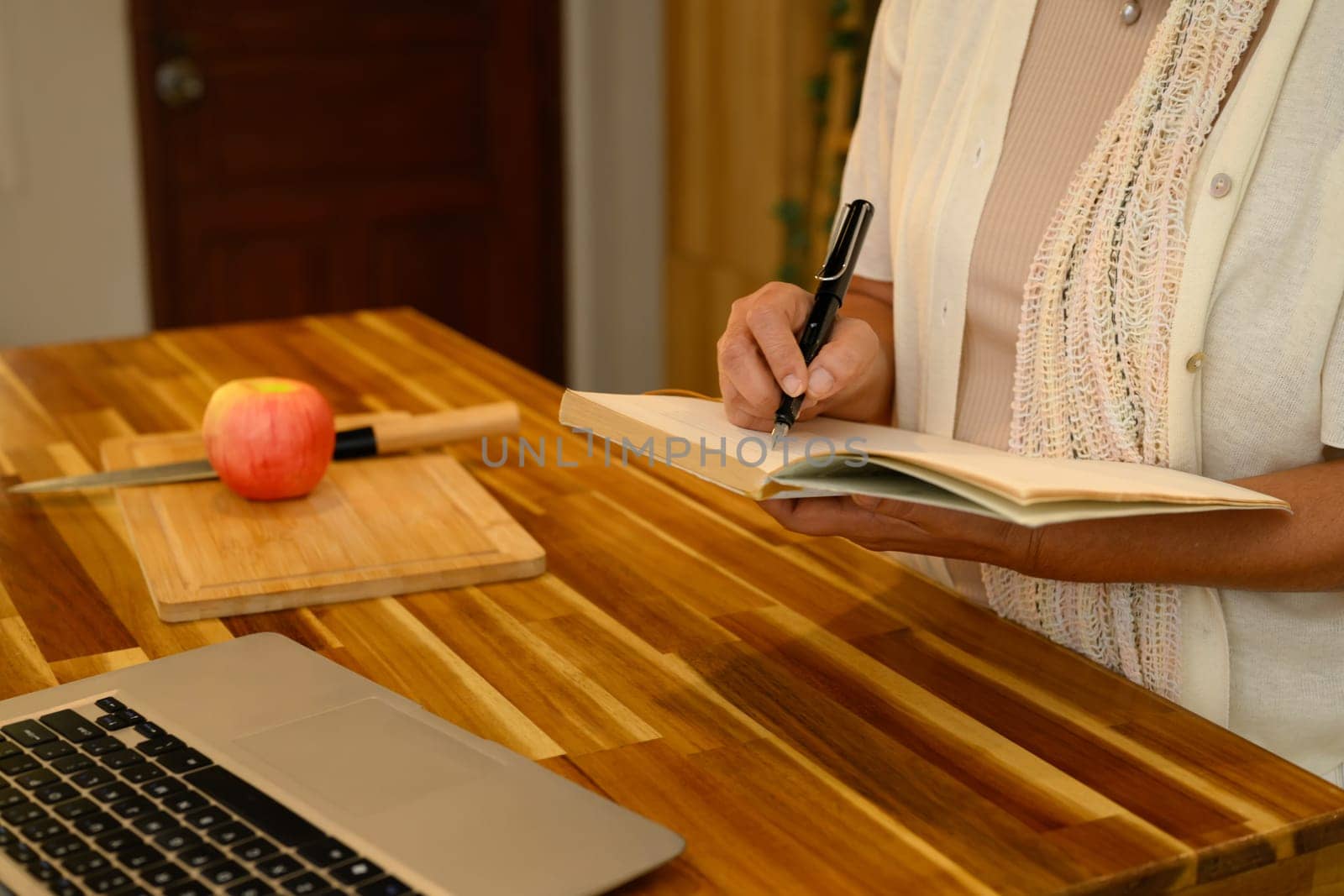 Cropped shot of senior woman learning and takes notes in a journal at wooden table.