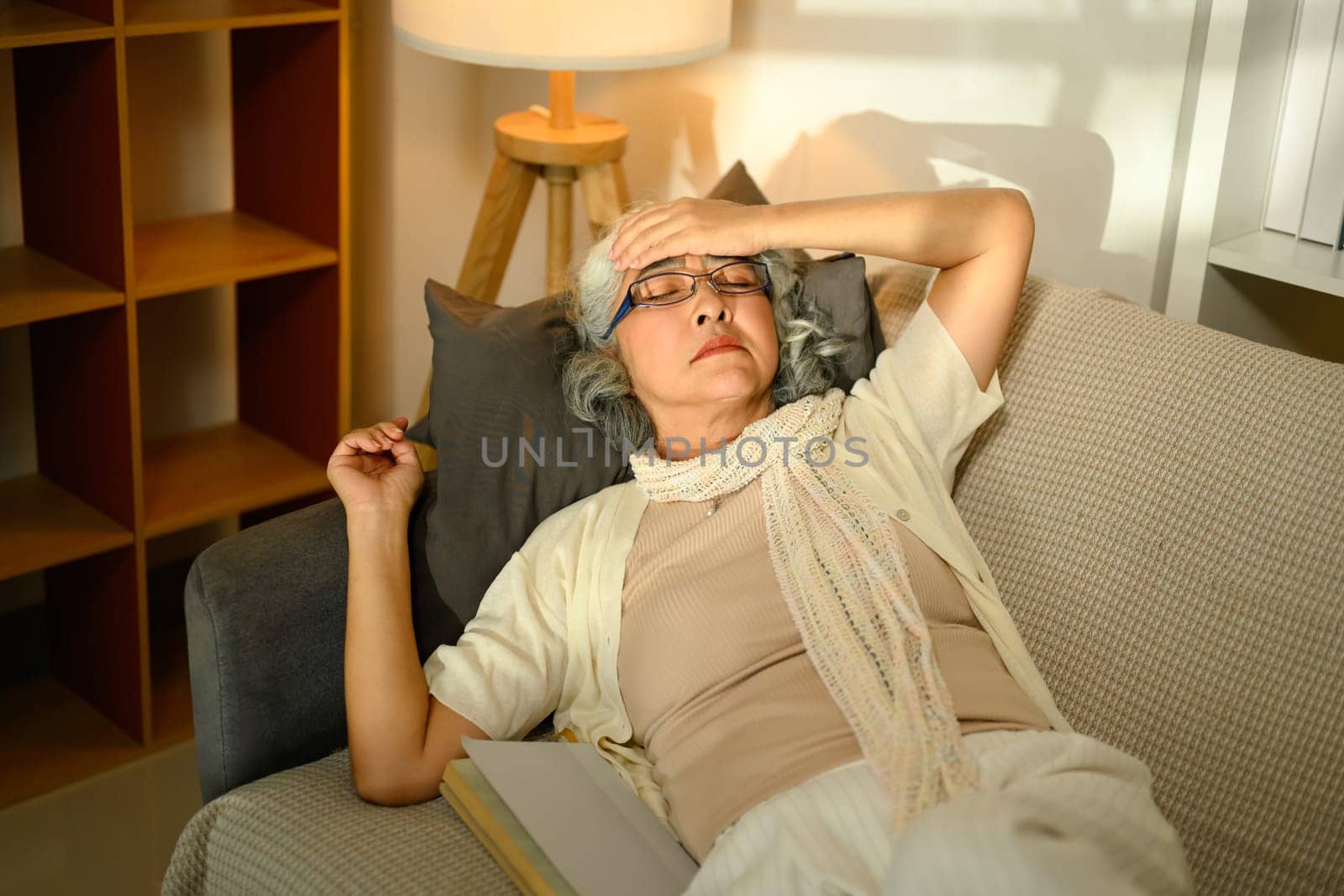 Sick senior woman lying back on sofa experiencing discomfort or headache. Health care concept.