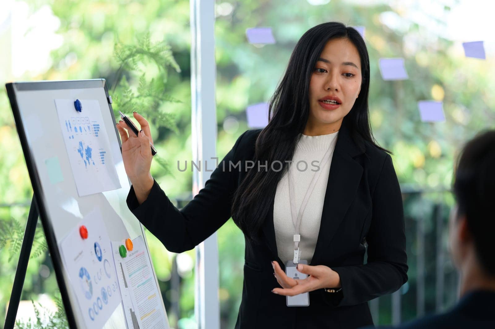 Confident businesswoman in a black suit presenting data on whiteboard during meeting.