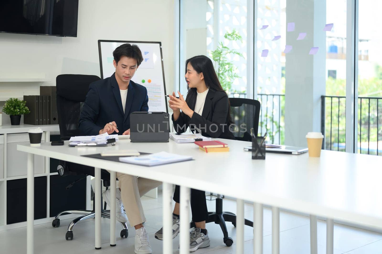 Two businesspeople dressed in formal suit working together on a project at bright office.