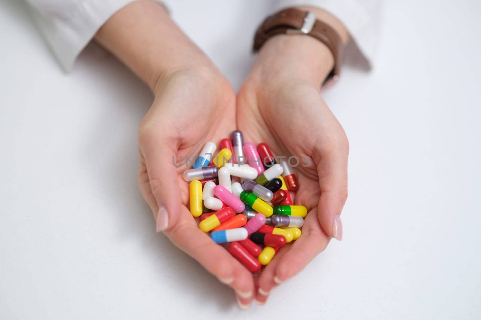 A detailed closeup image of hands holding a vibrant and varied collection of colorful pills and capsules