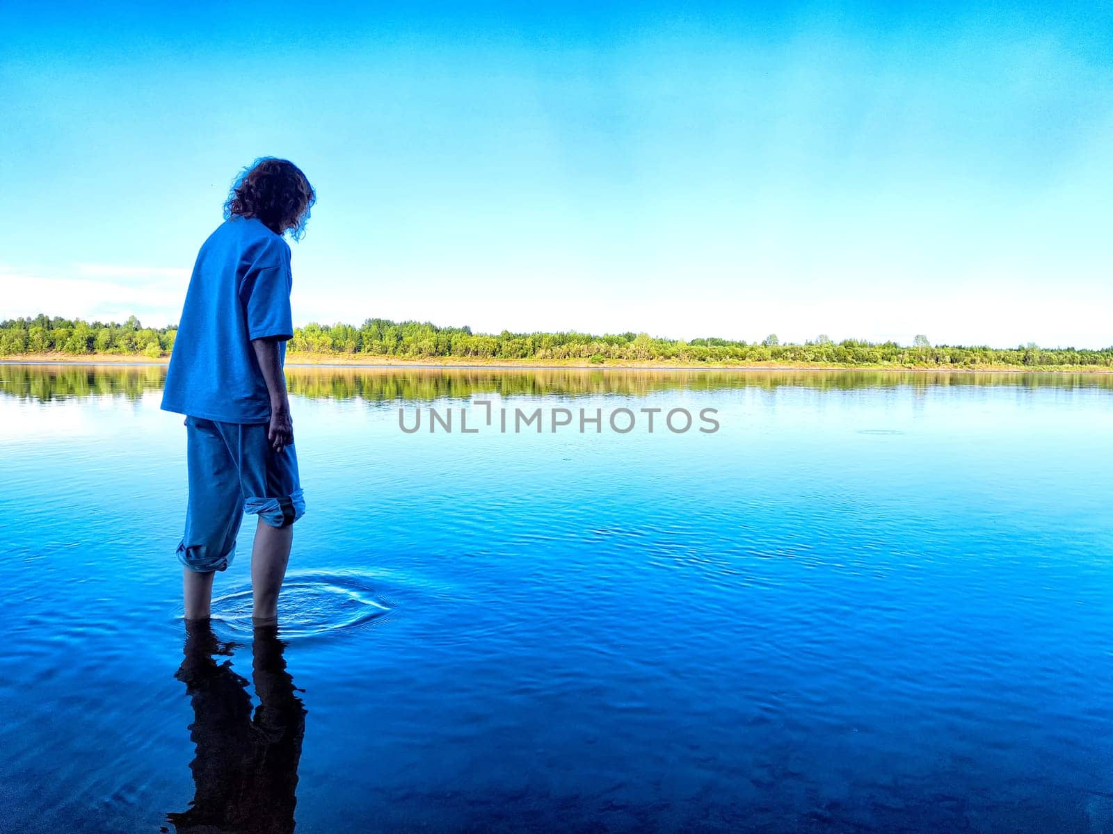 A tourist girl steps into the chilly water of a river, relishing the refreshing experience on a bright, beautiful day