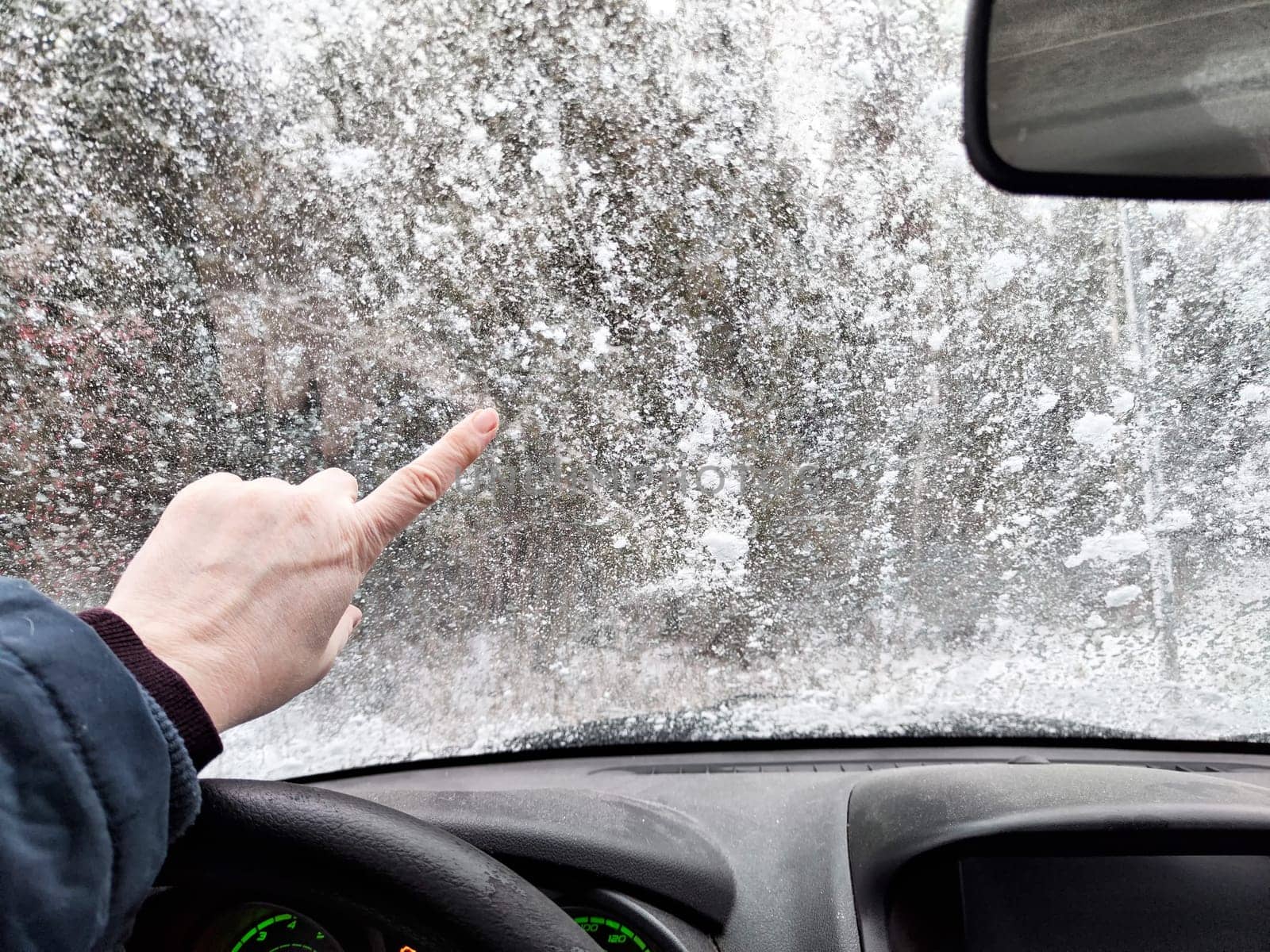A hand points out frost covering the car window while traveling on a cold winter day, showcasing the snowy scenery outside.