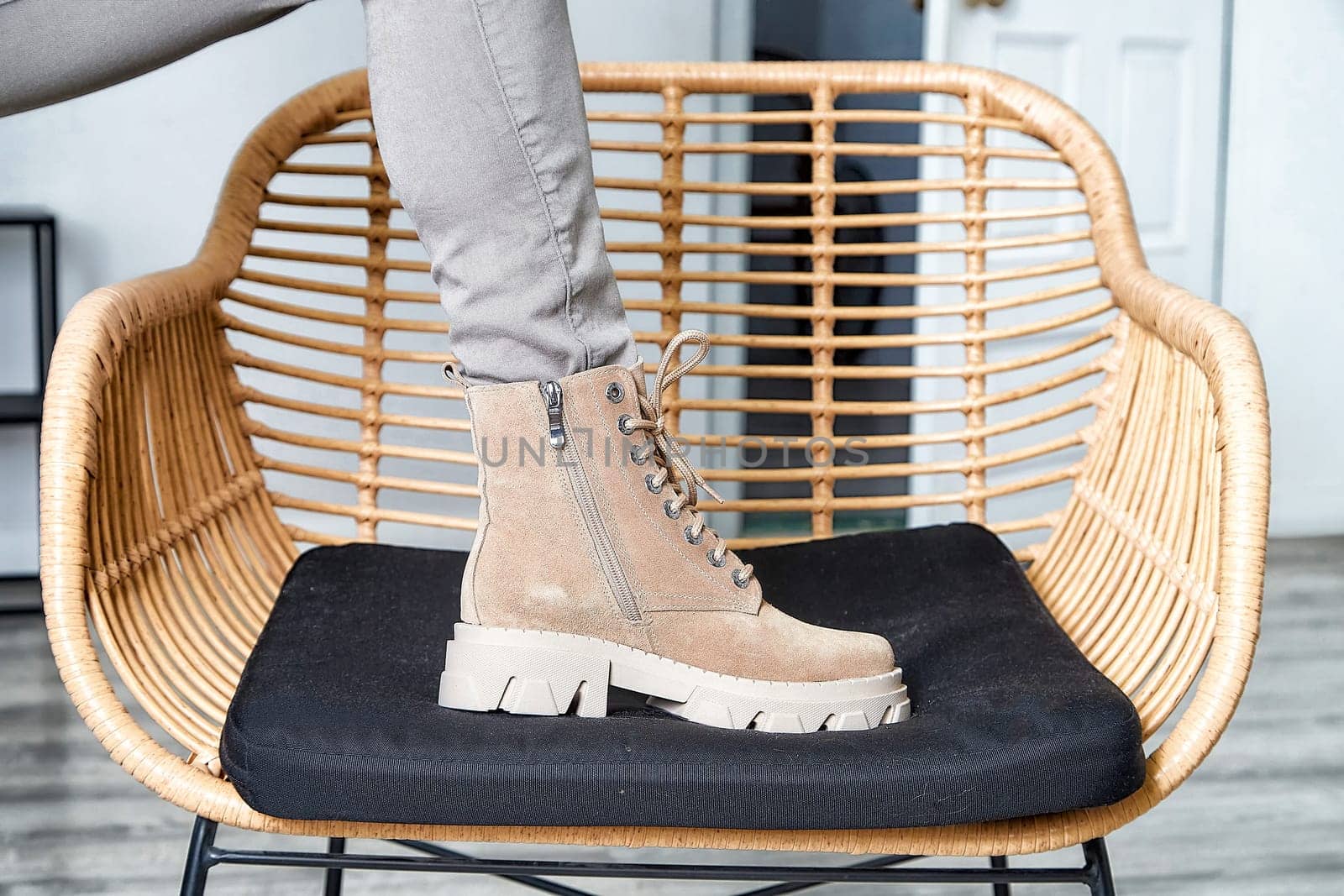 A model confidently poses with one foot on a stylish chair, highlighting trendy boots against a chic indoor backdrop.