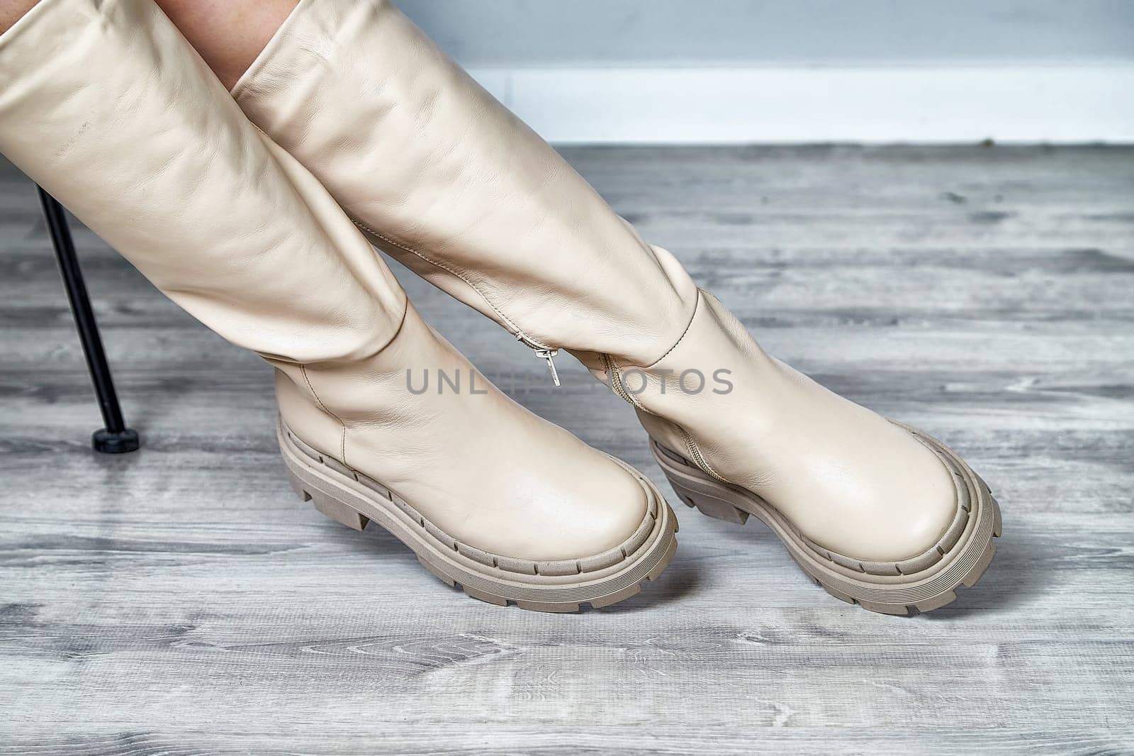 A model poses gracefully indoors, showcasing stylish beige knee-high boots that highlight contemporary fashion trends.