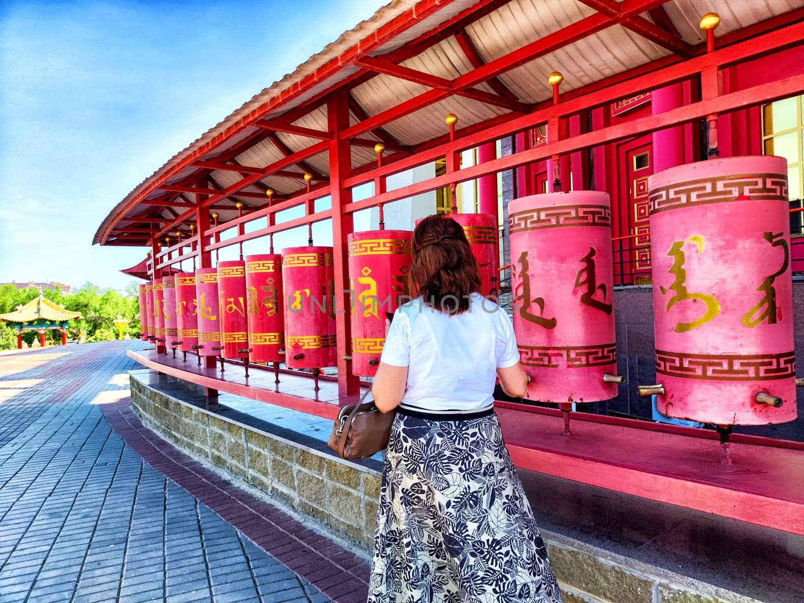 Elista, Russia - June 04, 2024: woman stands in front of prayer wheels, spinning them with her hand. Buddhism, temple, prayer, believer, faith