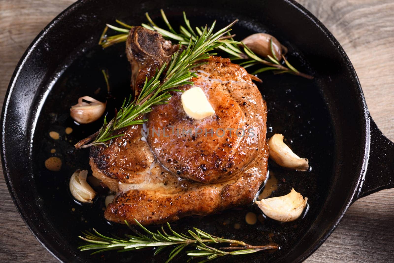 Pork cutlet on the bone in a piece of butter with garlic and rosemary in a frying pan 