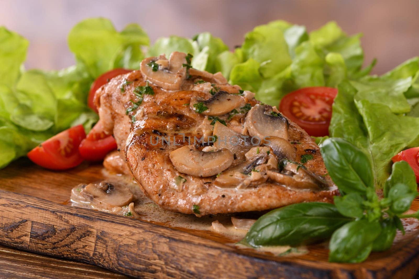 Chicken breast with mushroom sauce and vegetables on a wooden plate