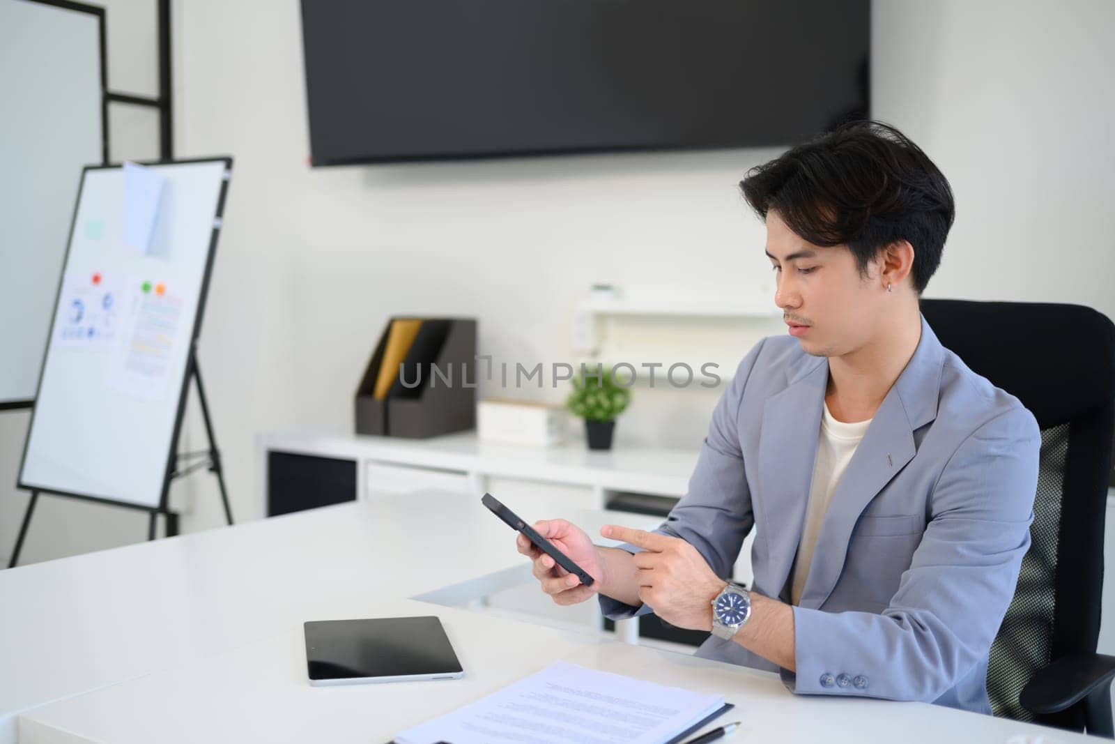 Young businessman using his smartphone to check data or messages at desk.