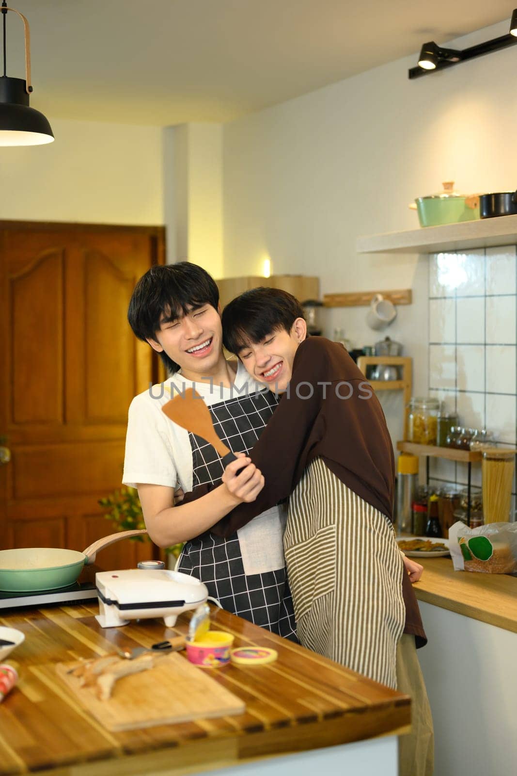 Loving male gay couple preparing a delicious breakfast at counter in warm kitchen.
