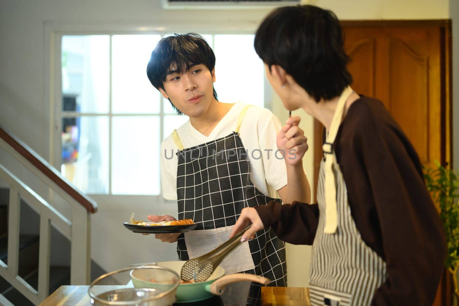 Happy gay couple enjoys cooking together in their home kitchen.
