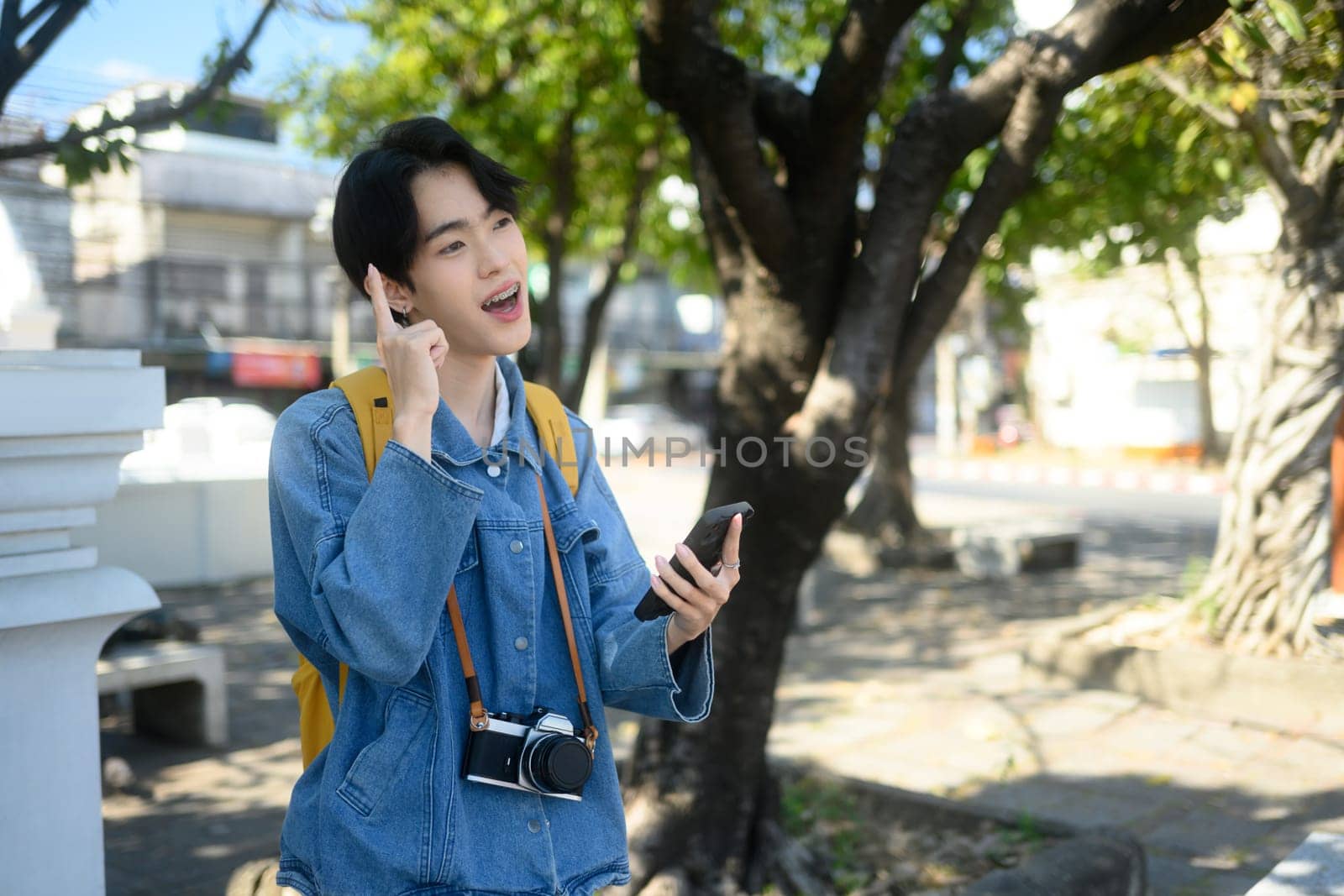 Young traveler with camera around their neck using mobile phone in a sunny urban. Exploration and travel concept.