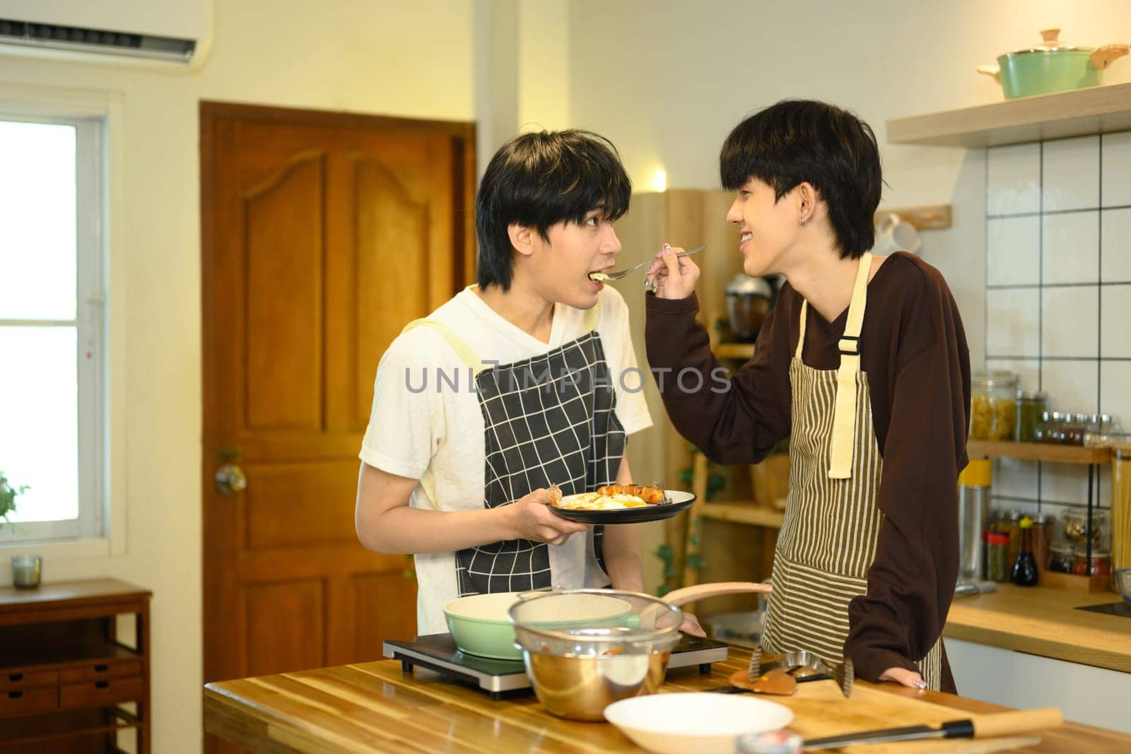 Loving male gay couple preparing a delicious breakfast at counter in warm kitchen.