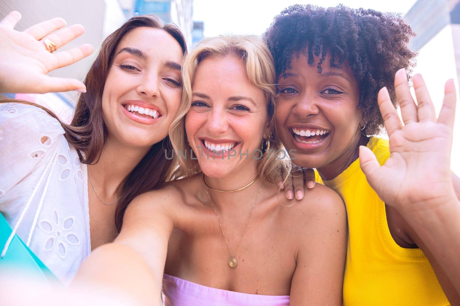 Three young women sitting outdoors, smiling, and taking a playful selfie together. Perfect for concepts like friendship, happiness, social media, and outdoor lifestyle.