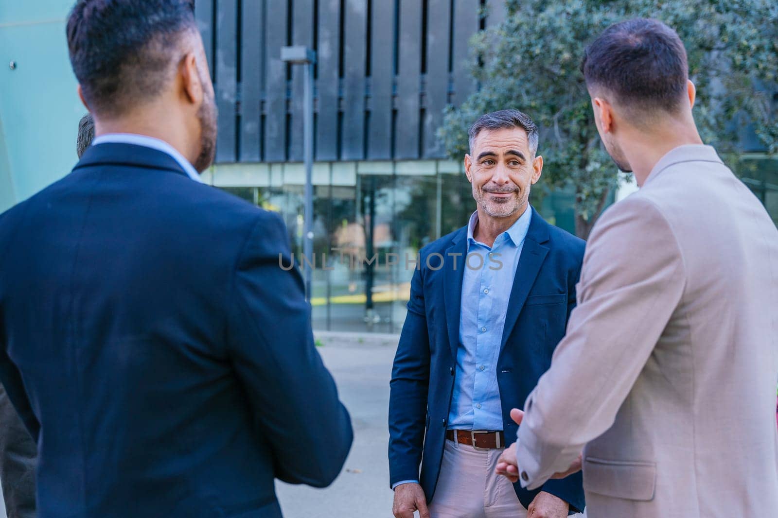 A group of business professionals engaged in a serious discussion outdoors. They are dressed in formal and smart casual attire, with a modern cityscape in the background.