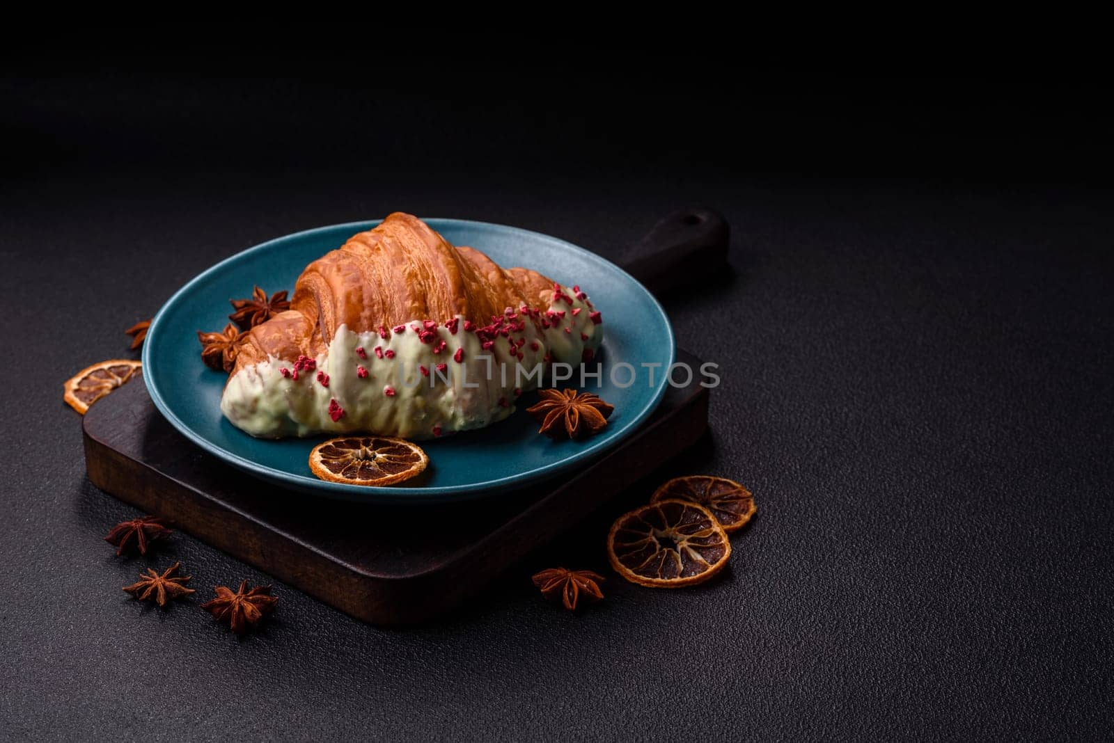 Crispy sweet red croissant with pistachio, raspberry and strawberry on a dark concrete background