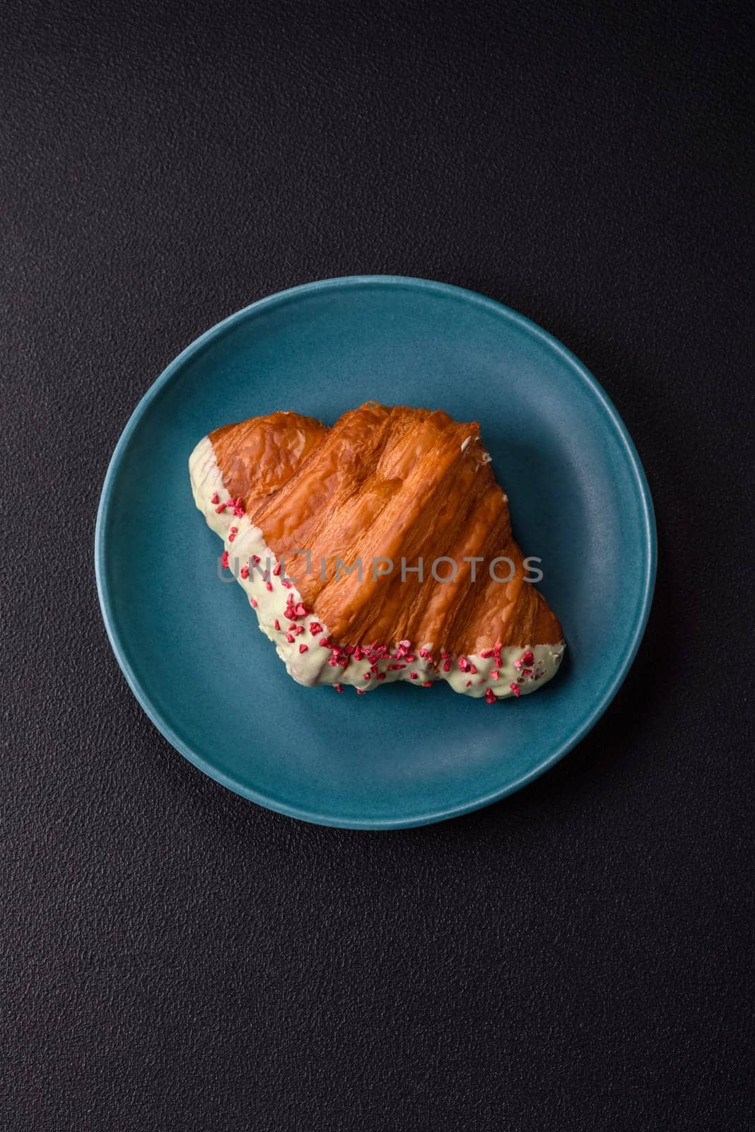 Crispy sweet red croissant with pistachio, raspberry and strawberry on a dark concrete background