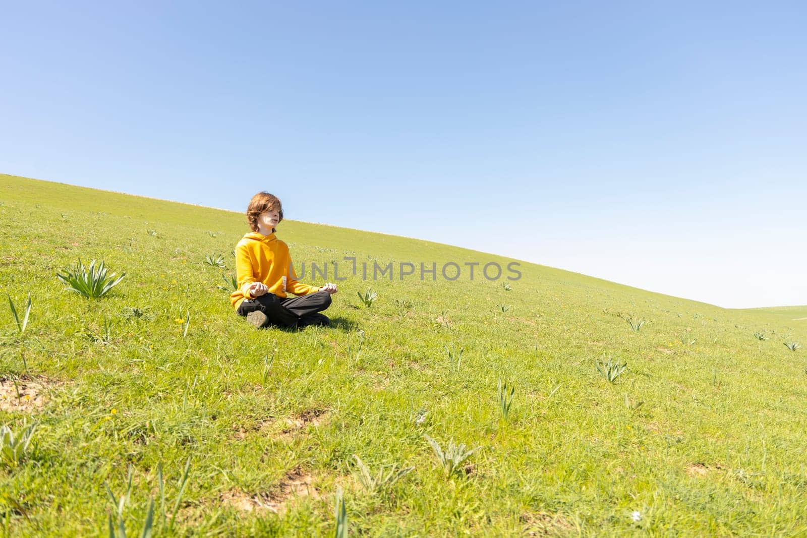 A young person sits peacefully on a green hillside. Tranquil and dreamy atmosphere. Peace and connection with nature.