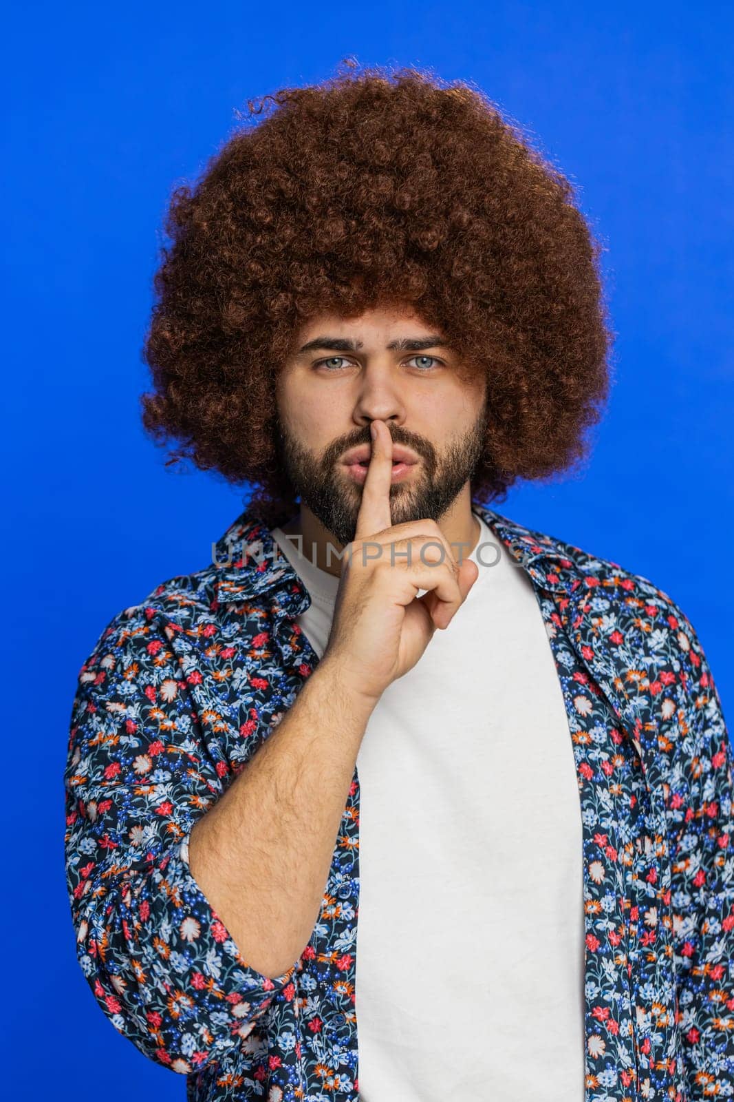 Shh be quiet please. Caucasian man presses index finger to lips makes silence gesture sign do not tells secret, stop talk gossip, confidential privacy. Stylish young guy isolated on blue background