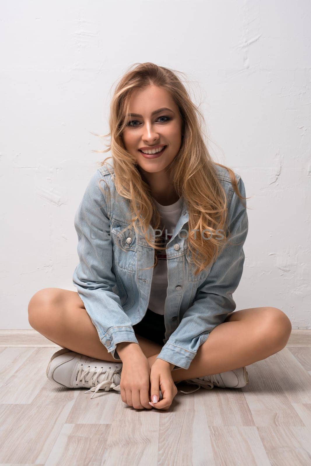Pretty happy blonde wearing jeans jacket sitting on the floor