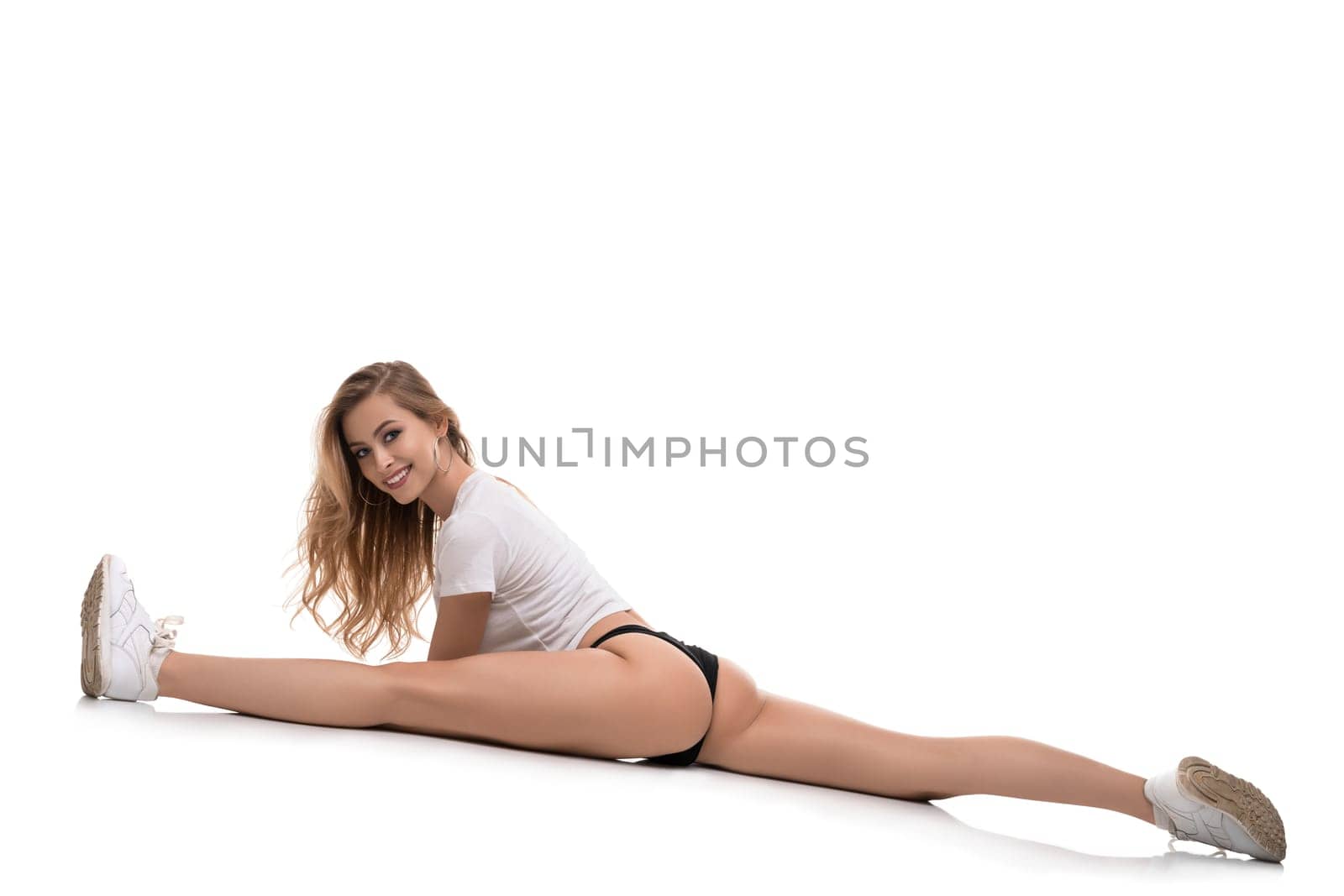 Sexy sporty blonde wearing black pants and top sitting in a split isolated rearview