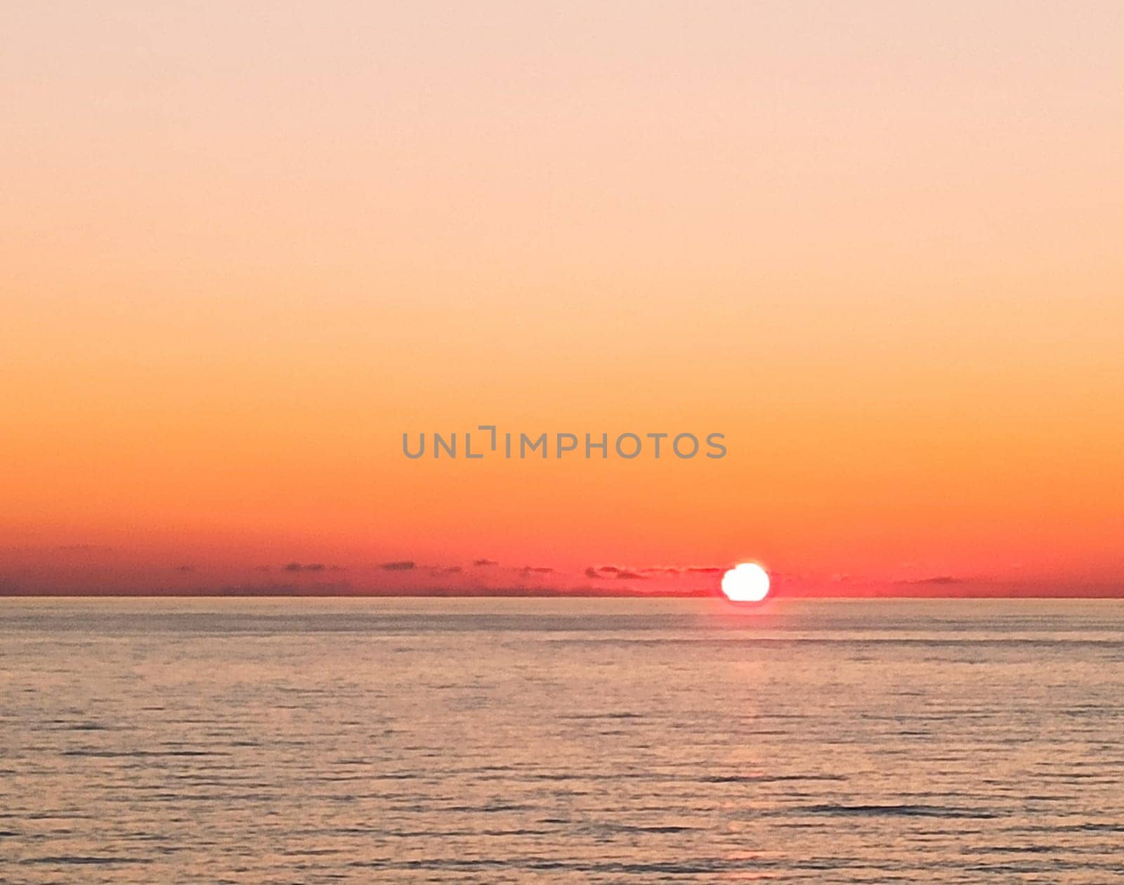 A stunning sunset casts warm hues across the ocean as the sun sinks toward the horizon. The tranquil water mirrors the vibrant colors, creating a serene atmosphere.
