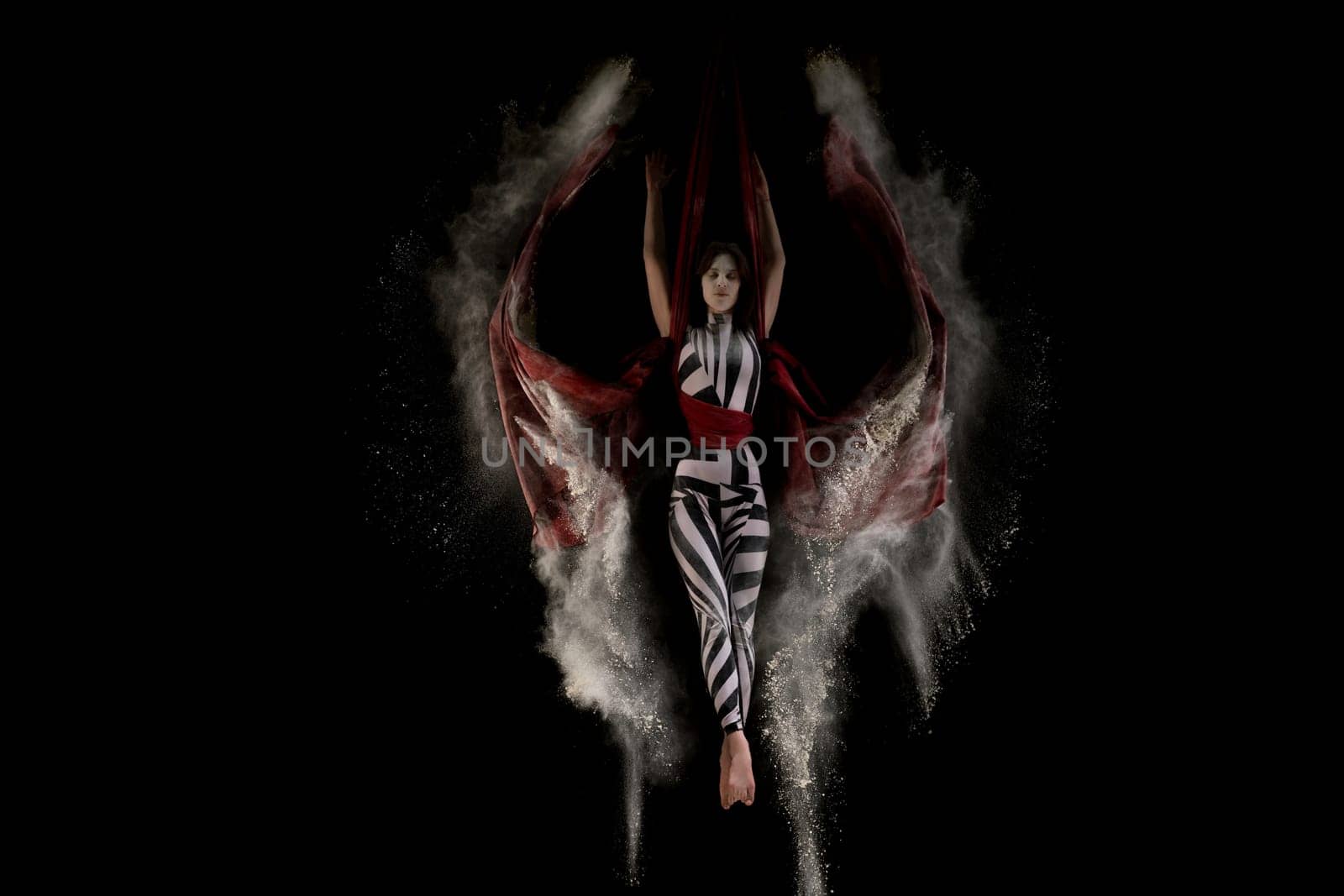 Beautiful woman wearing striped body dancing on cloth in white dust cloud shot in the dark