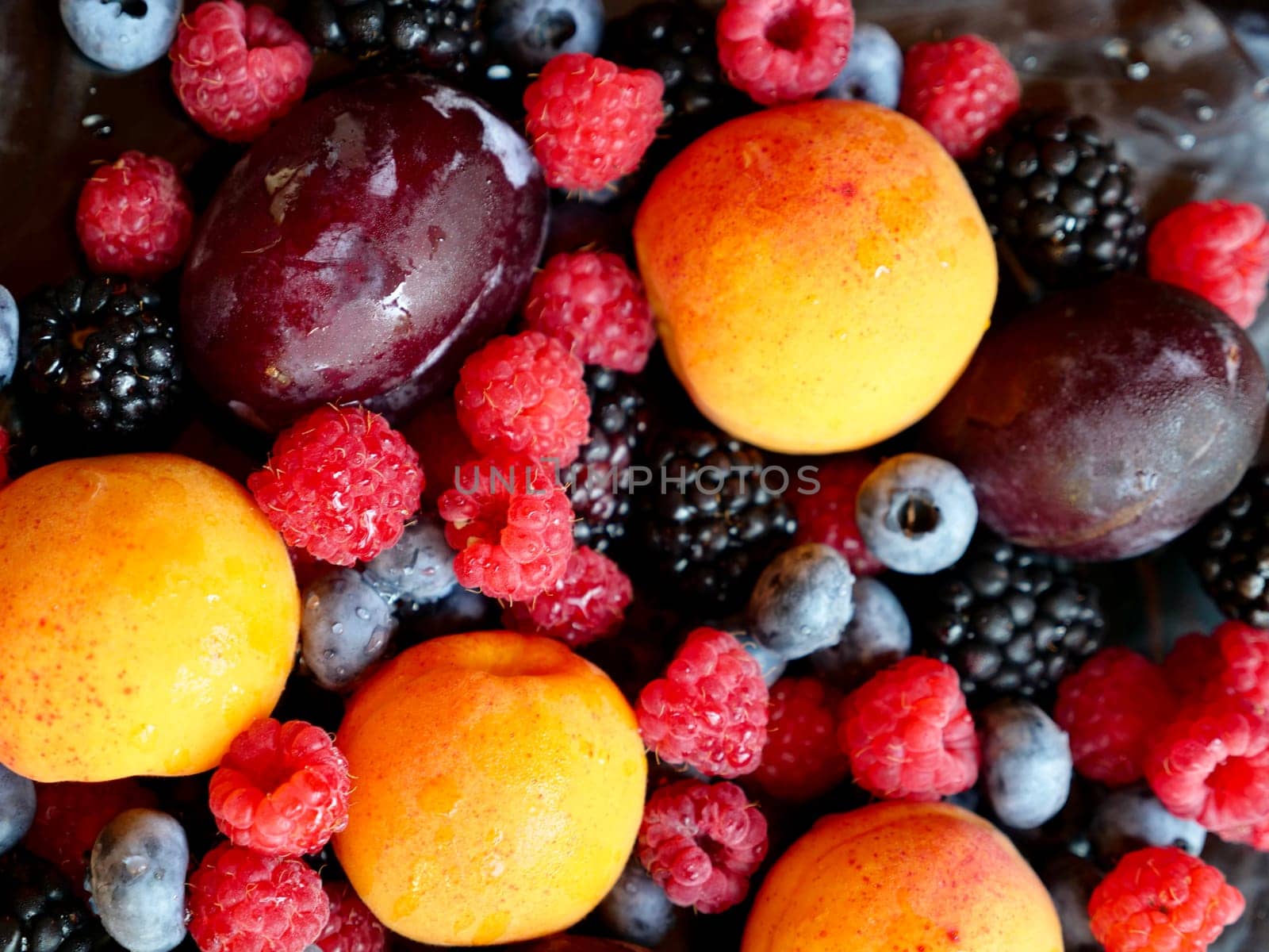 Colored background of seasonal summer fruits apricot, plum, raspberry, blueberry, blackberry in garden, close up