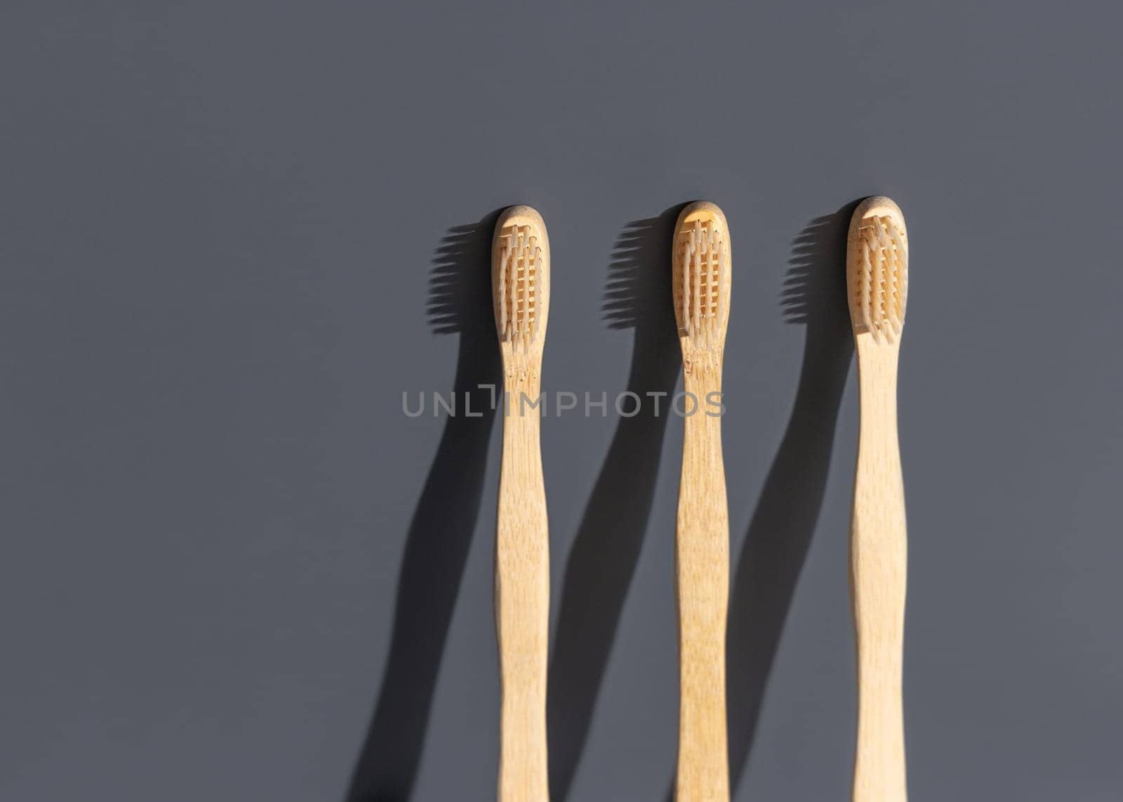 Beige biodegradable bamboo toothbrushes on a grey background with hard shadow closeup, mockup, negative space. Natural personal accessories for dental care, minimal style aesthetic