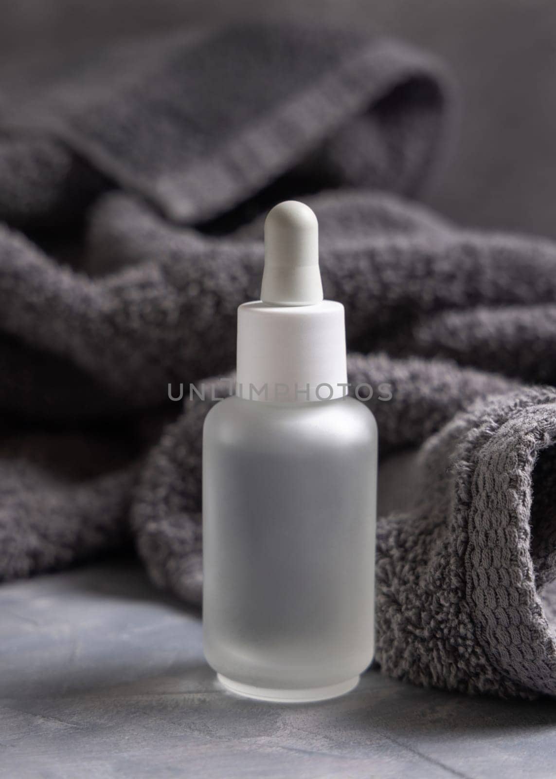 Clear glass dropper bottle with pipette near dark grey towel closeup, brand packaging mockup, copy space. Natural handmade cosmetic product for facecare and spa procedures - serum or essence