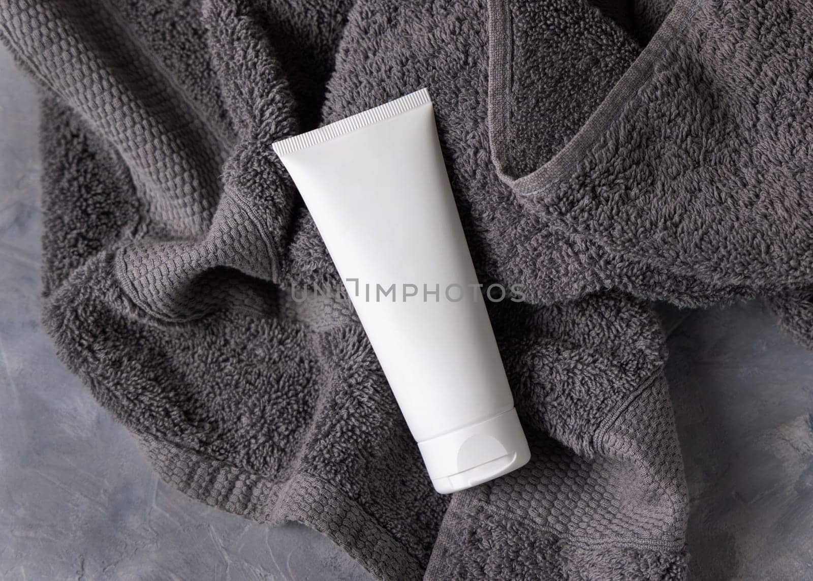 White blank cosmetic squeeze cream tube on dark grey towel in bathroom top view, brand packaging mockup. Natural handmade cosmetic product for facecare, copy space