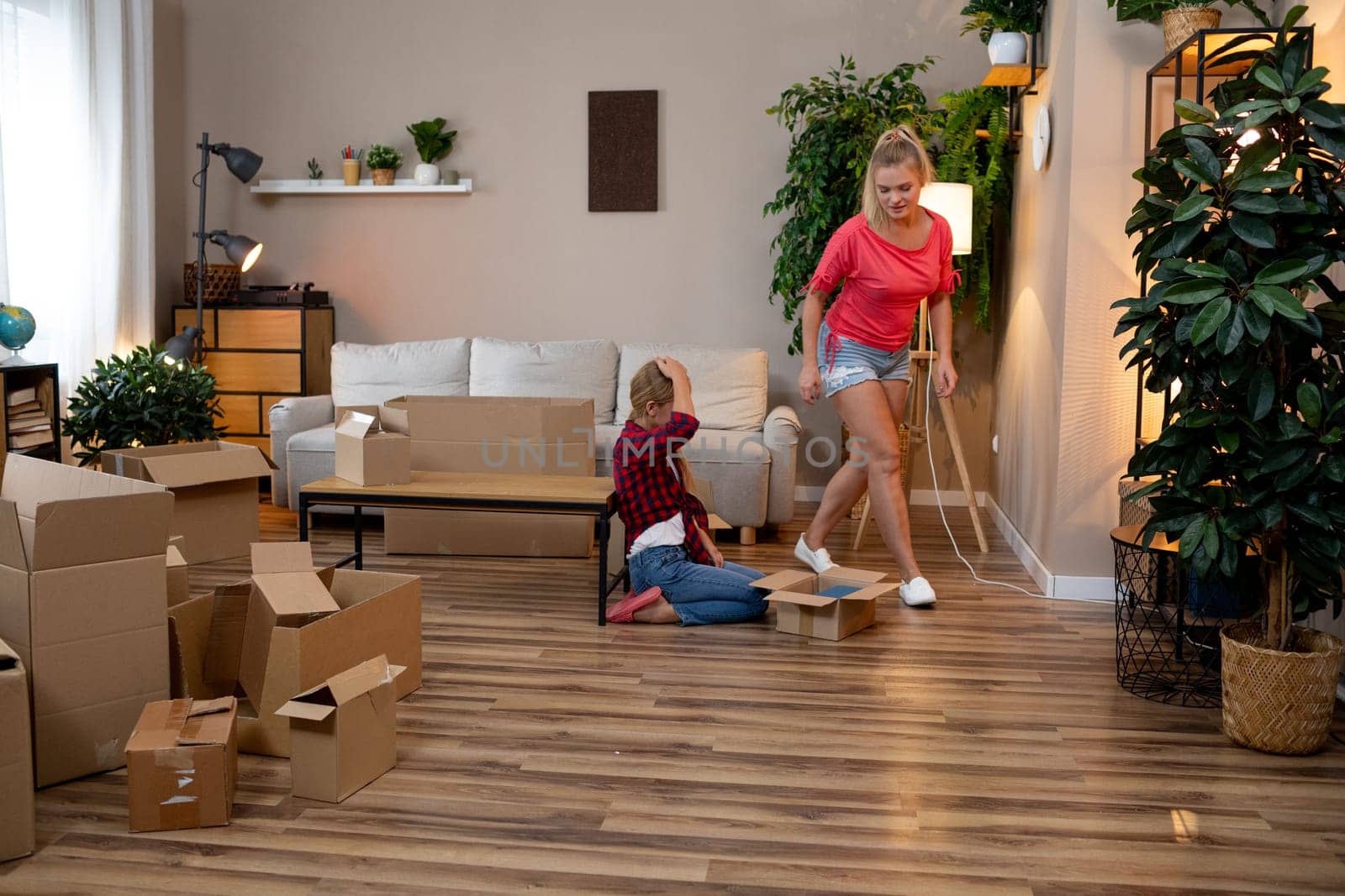 In a cozy living room with greenery, a mother and child happily unpack boxes, enjoying each others company