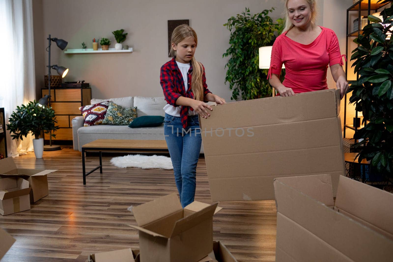 A delighted child and a caring adult cheerfully unpack a variety of cardboard boxes in a cozy living room setting