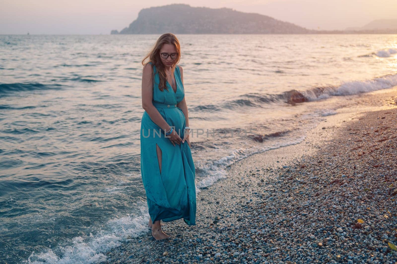 A woman in a flowing green dress poses on a pier by the sea at sunset, with a Turkey flag waving in the background.
