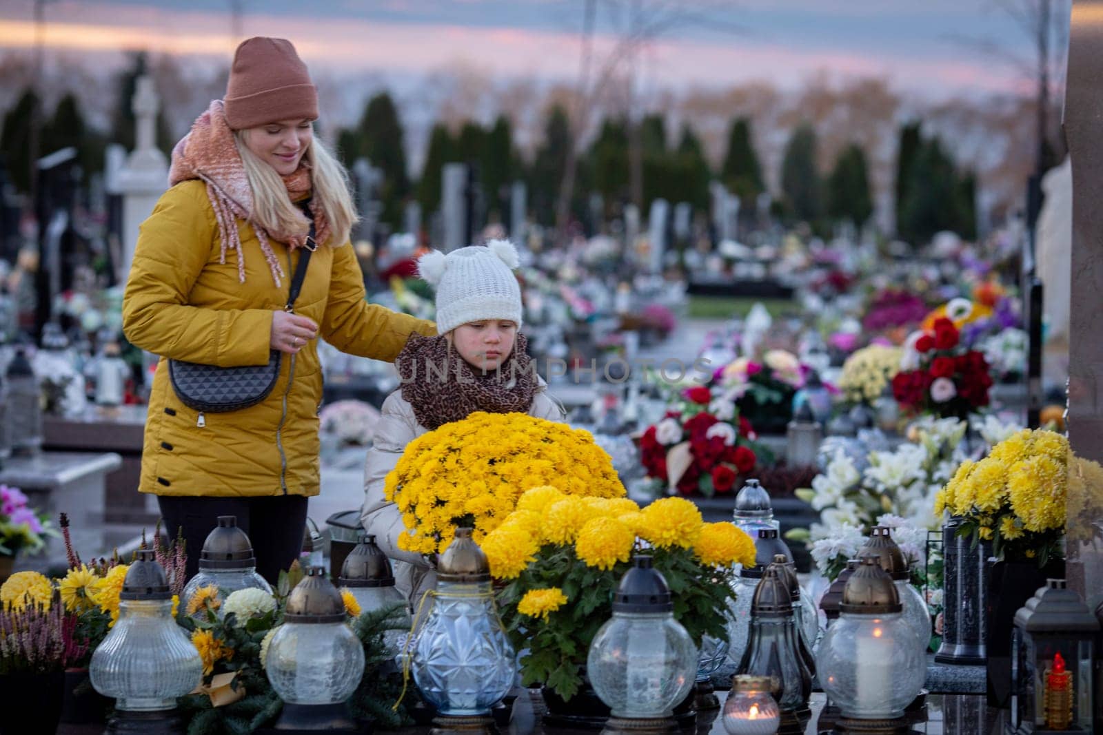 In a tranquil cemetery, a touching moment of remembrance unfolds, showcasing a mother and child amidst floral tributes