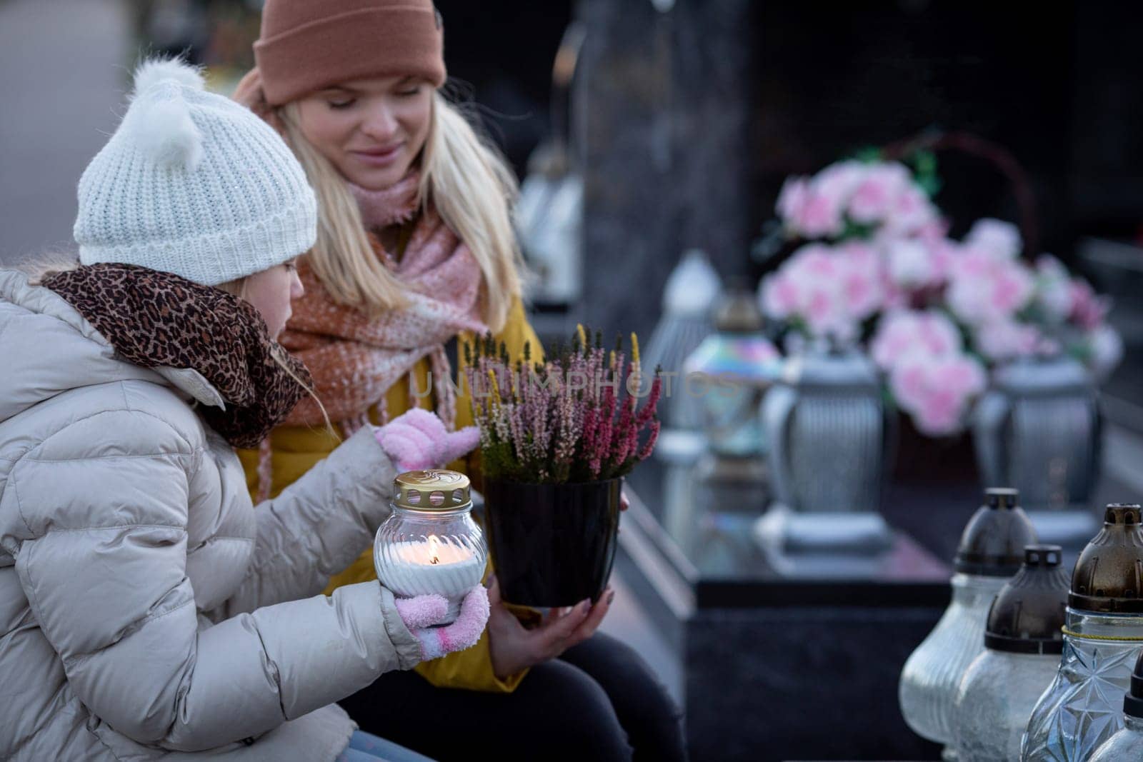 Two women gather at a peaceful cemetery, honoring loved ones with lanterns and fresh flowers placed gently