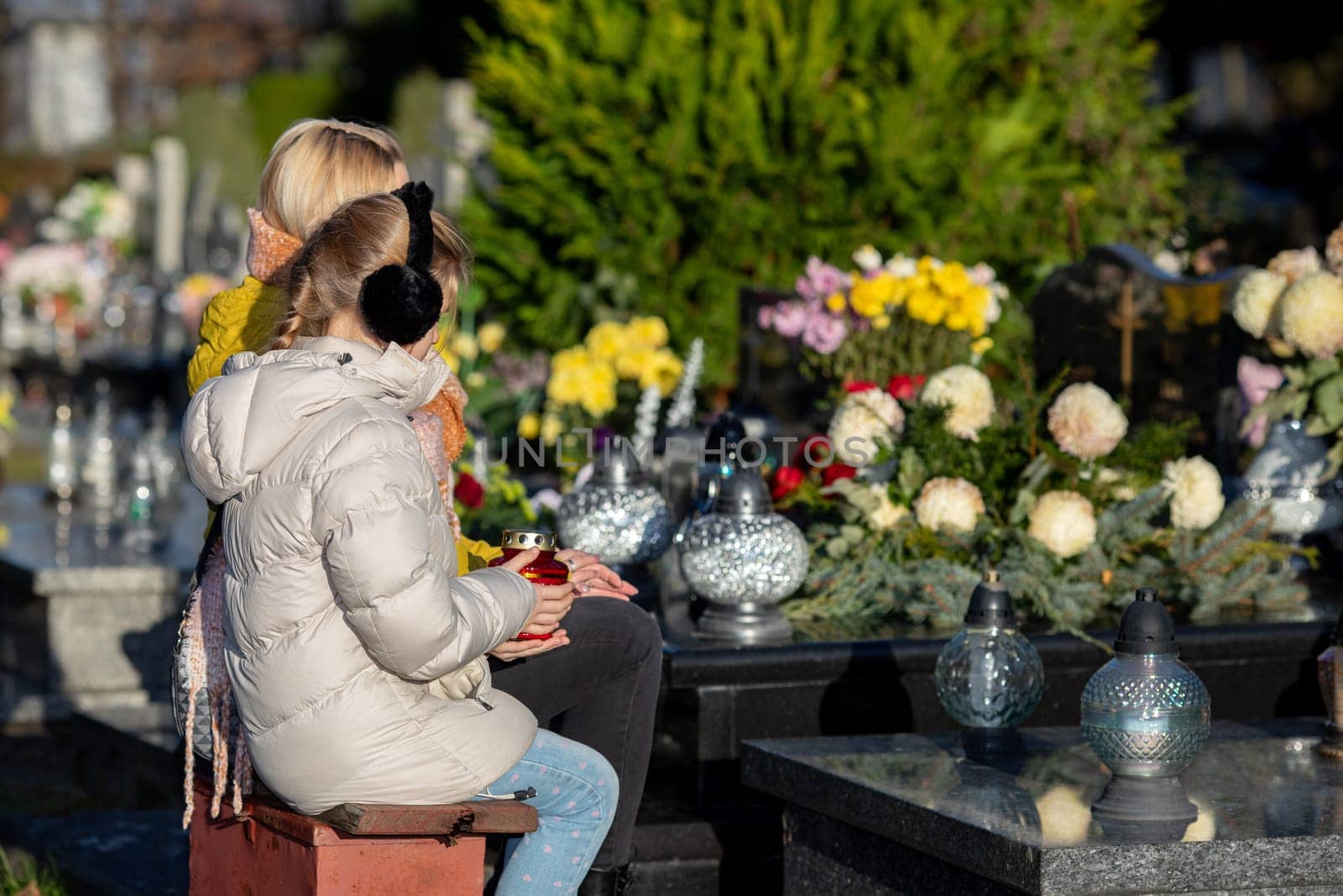 Two individuals reflect on their loved ones among vibrant flowers in a serene cemetery, filled with memories
