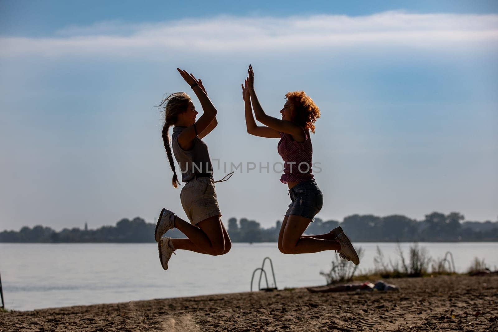 Two friends are enjoying a carefree and blissful moment as they joyfully jump together by the serene lake