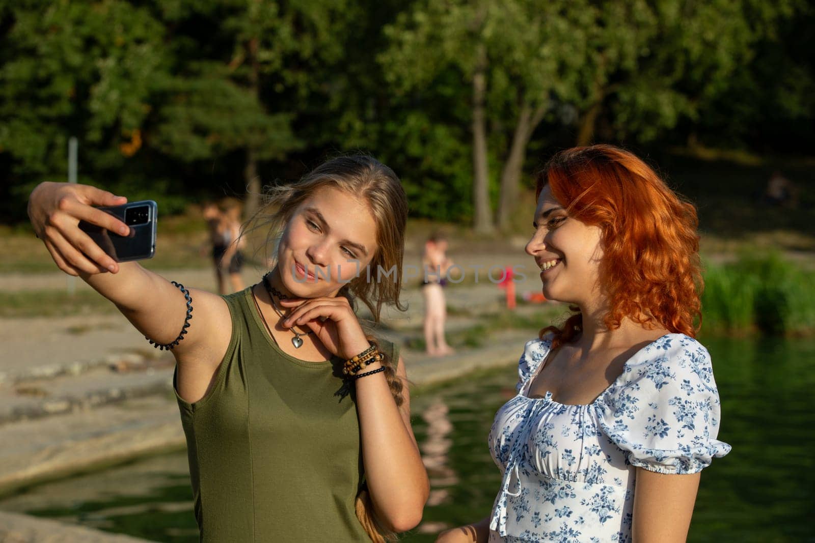 Two close friends are enjoying a bright and sunny day while capturing wonderful memories with a fun selfie by the water
