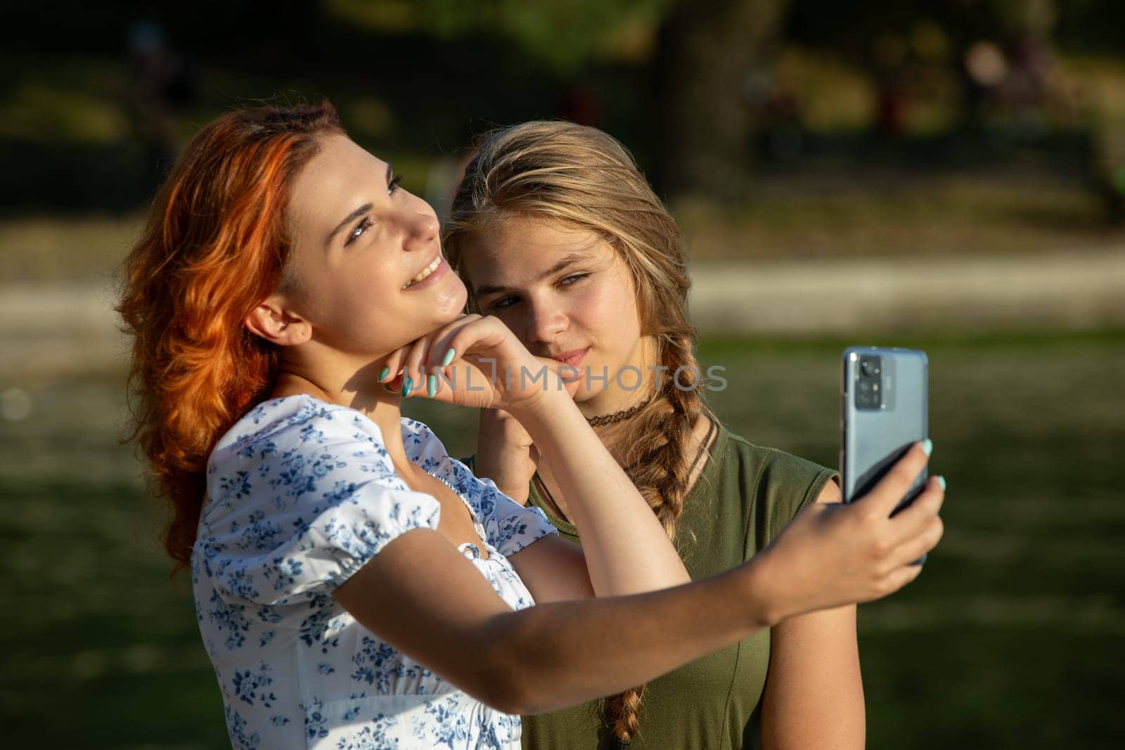 Two close friends share a joyful moment capturing a selfie by the water in a sunny park on a beautiful day