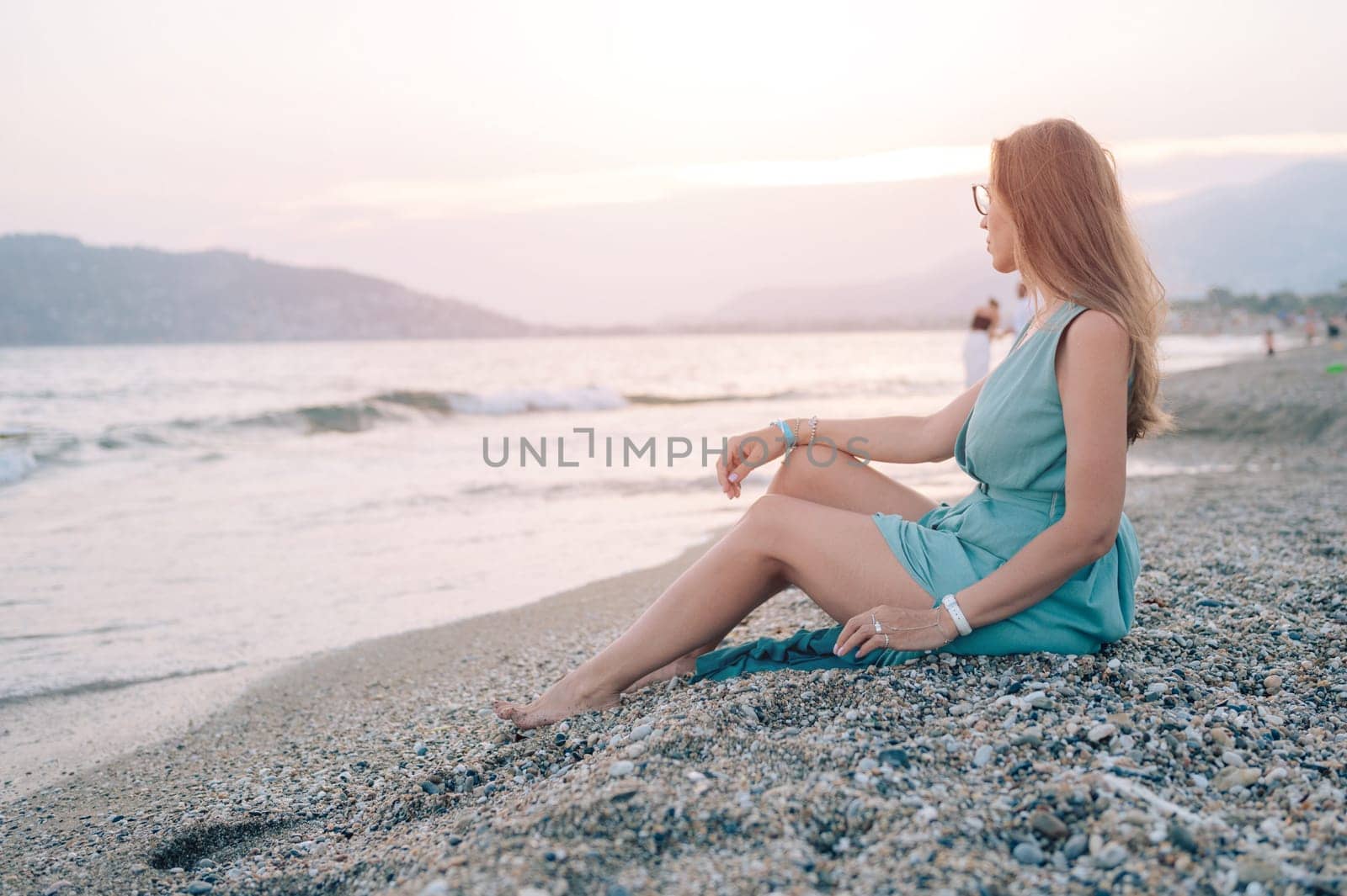 A woman in a flowing green dress poses on a pier by the sea at sunset, with a Turkey flag waving in the background.