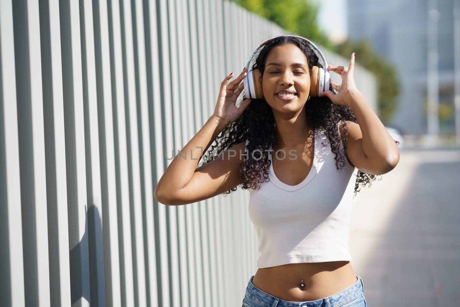 A cheerful young woman is joyfully dancing to her favorite upbeat music, while wearing stylish headphones in a vibrant urban setting that captures her love for music and the freedom it provides her