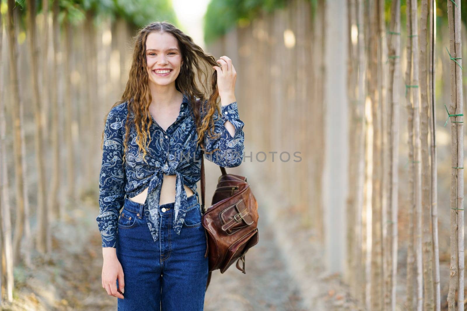A joyful young woman stands gracefully among lush greenery, dressed in a stylish outfit and beaming with a radiant smile, embodying happiness and confidence for lifestyle and fashion themes