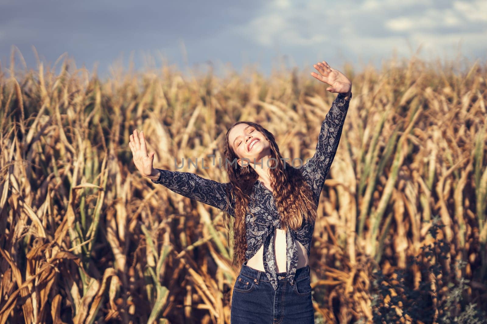 In a vibrant cornfield under golden sunlight, a joyful young woman dances with her arms raised, radiating happiness and freedom through her energetic, playful movements, spreading positivity