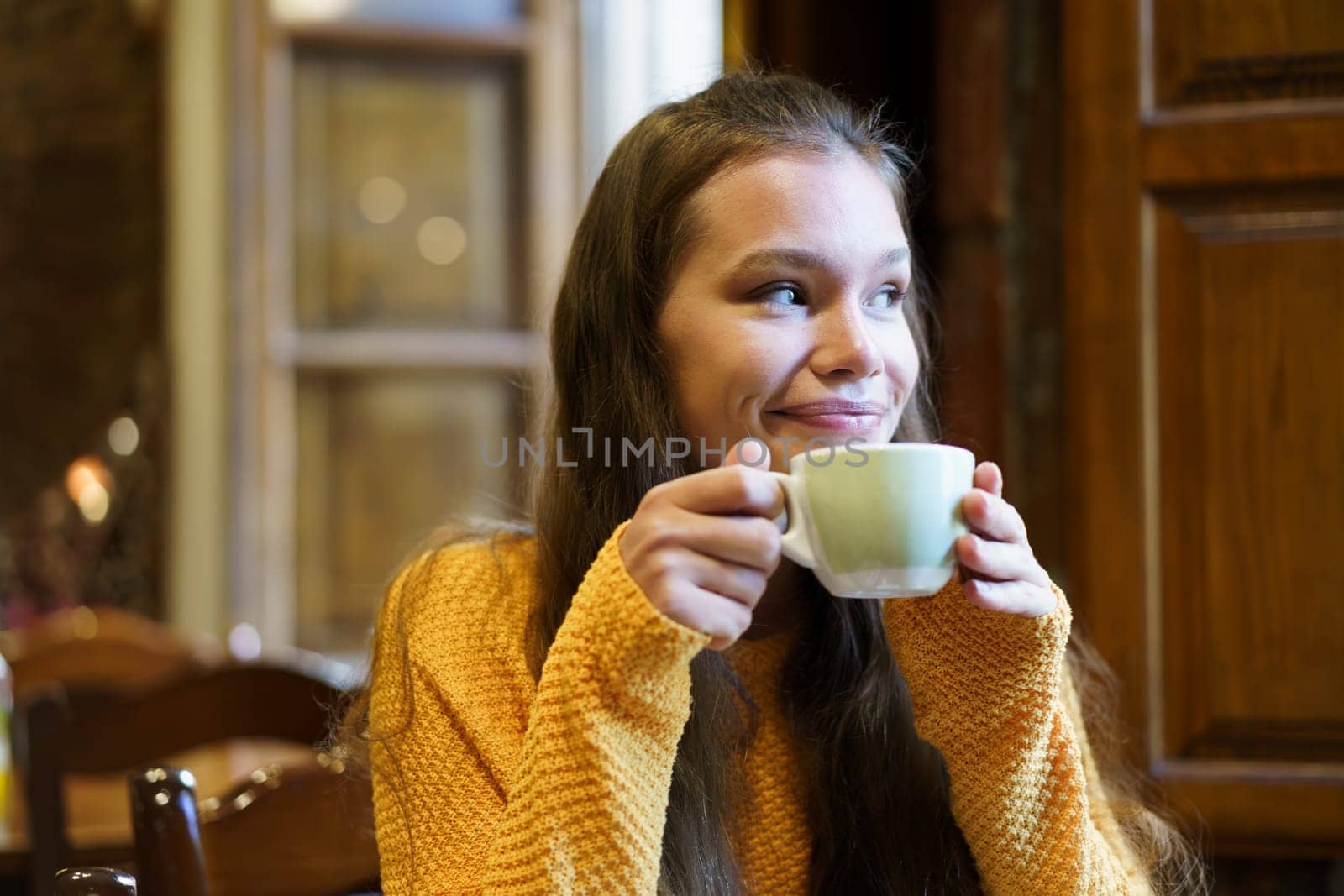 A young woman savors a warm cup of tea or coffee in a charming caf, radiating joy and relaxation