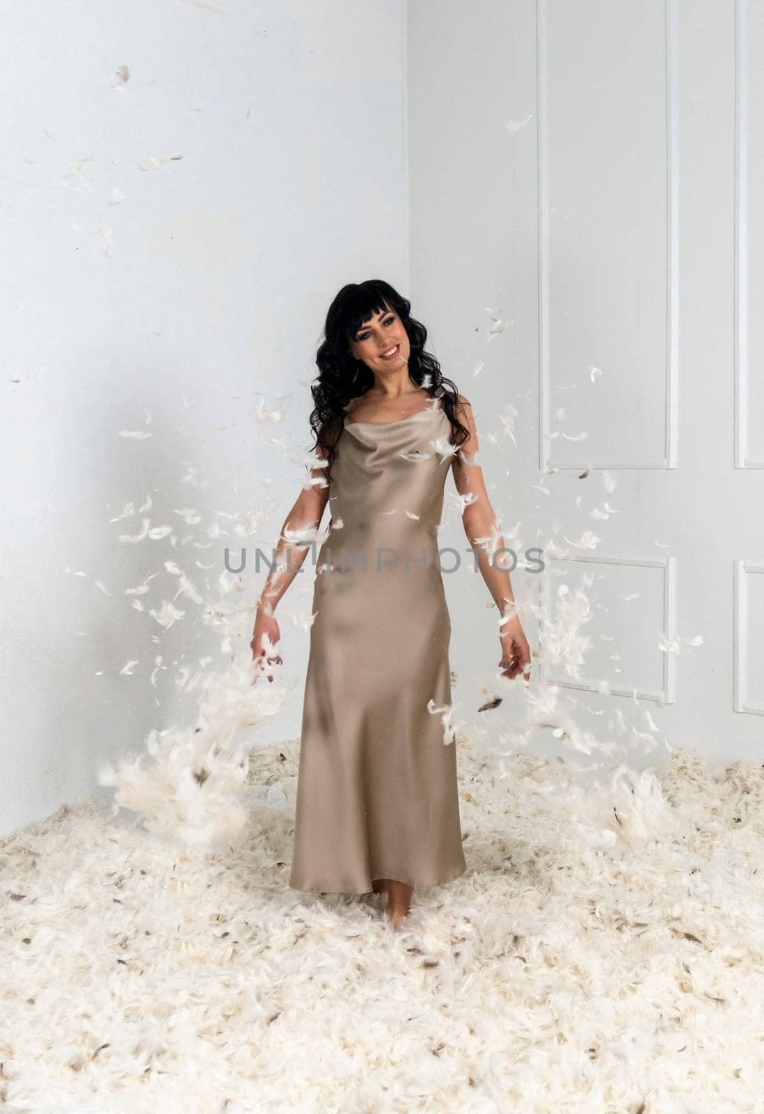 beautiful slender girl white feathers are flying around her. brunette girl with long hair. she is standing in a white room there are many white feathers around her. feathers are flying around her.