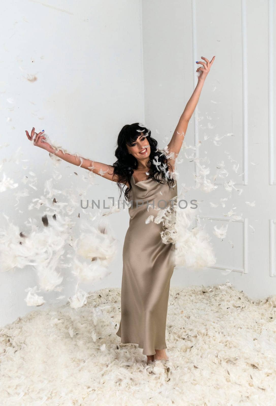 beautiful slim girl throws white feathers. she is standing in a white room around her many white feathers. feathers are flying around her. girl with both hands threw feathers into the air