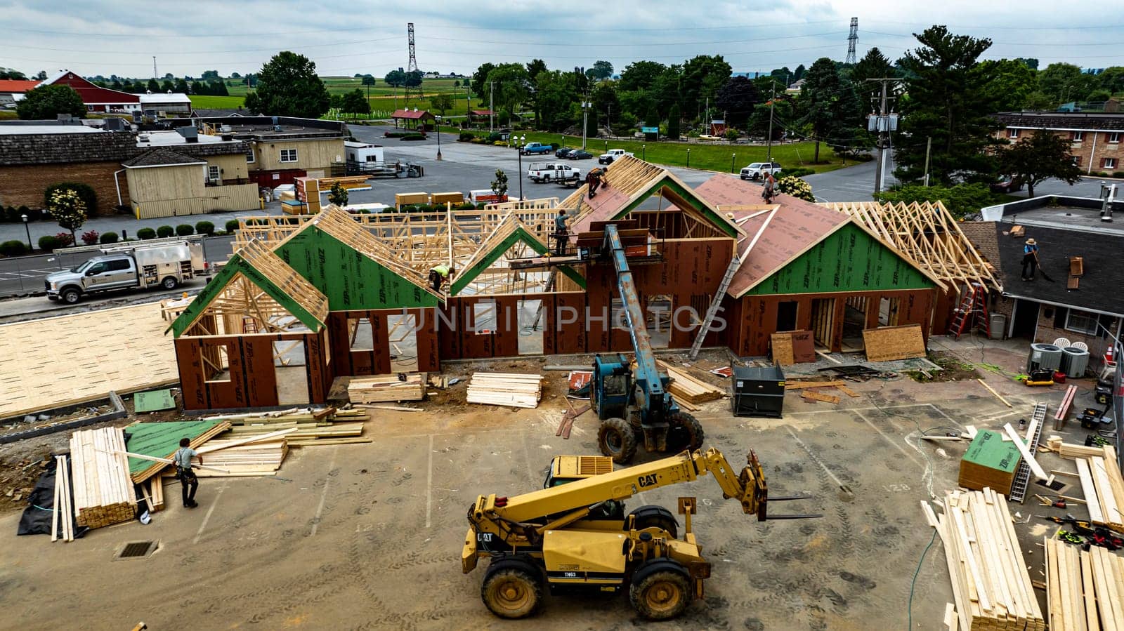 Bird in Hand, Pennsylvania, USA, June 6-2024 - Aerial View Of A Busy Construction Site With Wooden Framing And Building Materials On A Sunny Day, Surrounded By Green Fields, Residential Buildings.