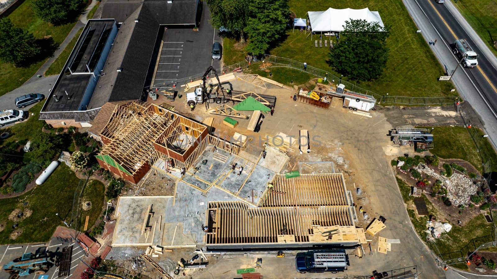 A construction project is progressing with workers actively framing a new building at a commercial location. The structure has wooden frames and is set amidst a clear sky and green landscape.