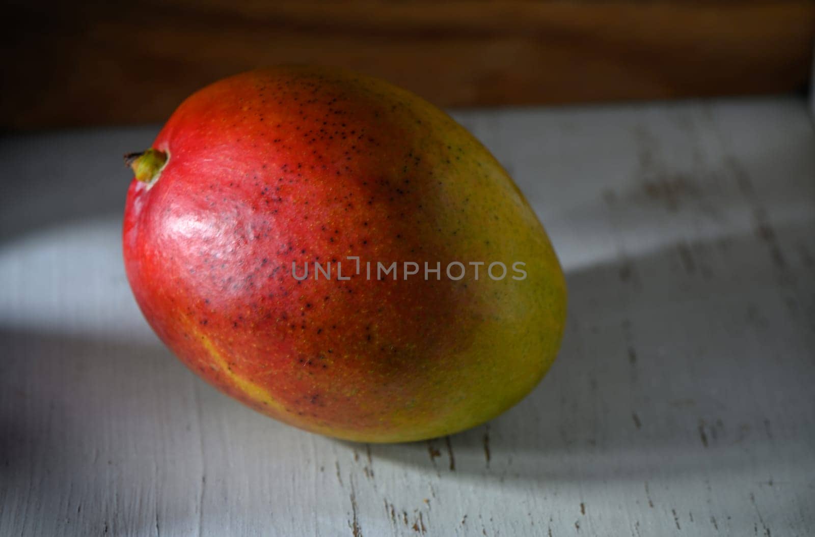 Ripe mango rests peacefully on a weathered wooden table, illuminated by golden afternoon sunlight.